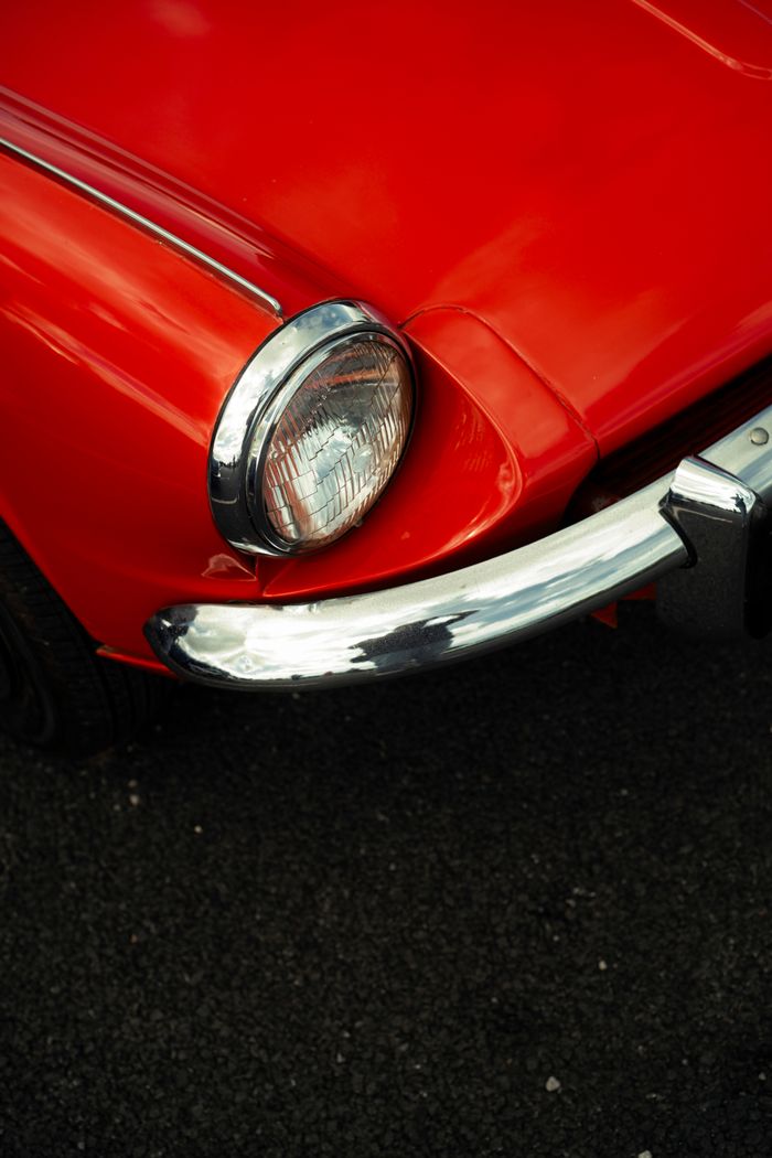 Detailed view of a classic red cars headlight and chrome bumper.